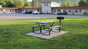 Ein Picknicktisch mit Bänken in einer Rasenfläche vor einem Motel, auf dessen Zufahrt mehrere Autos parken.