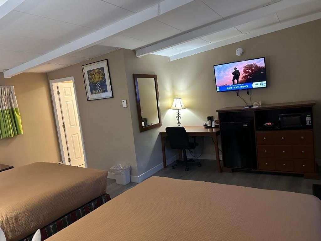 Habitación de hotel con cama, escritorio, silla, televisor y cómoda.