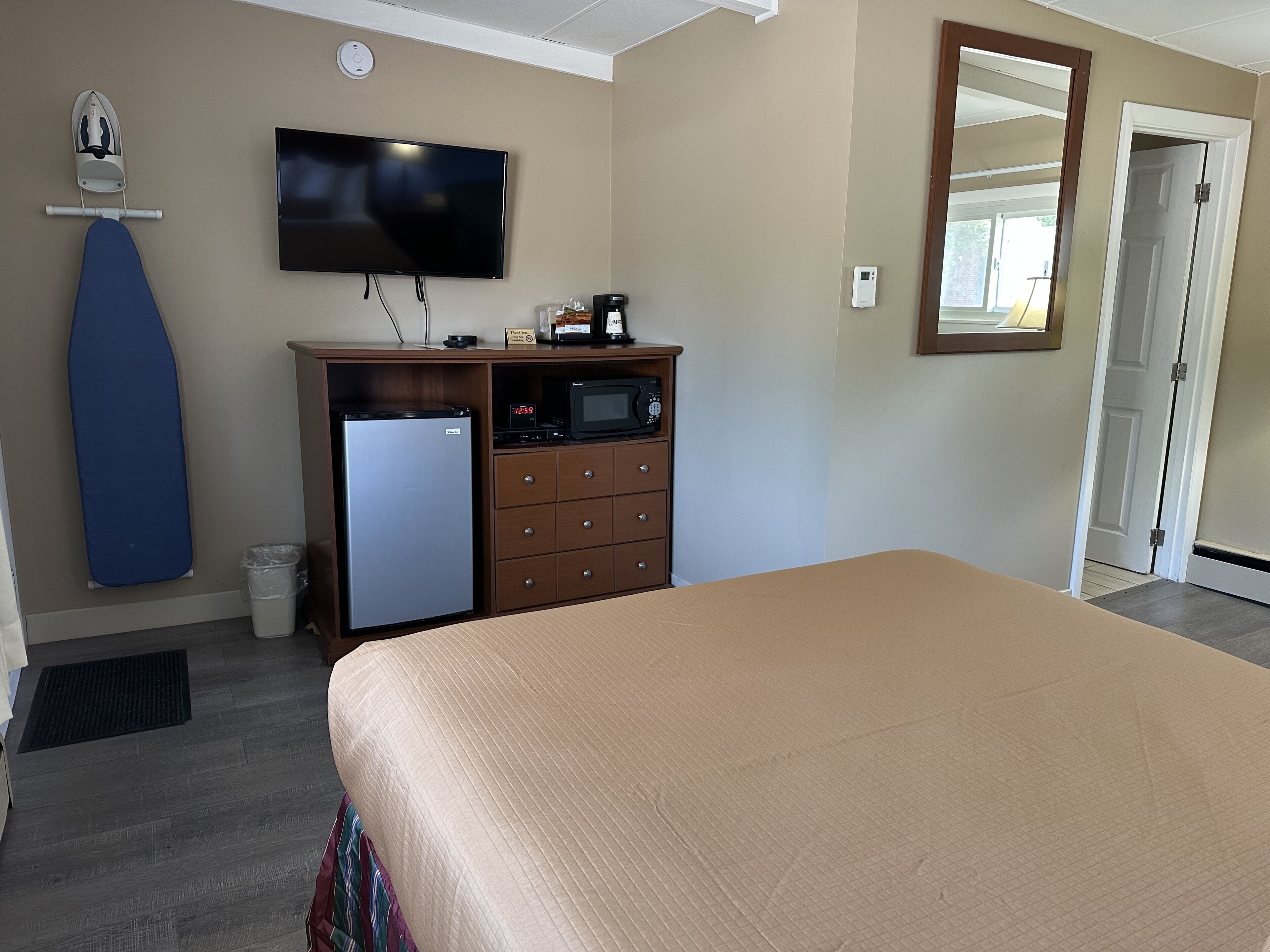 A hotel room with a bed, a TV mounted on the wall, a microwave, a refrigerator, a dresser, and a door.