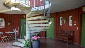 Un escalier en colimaçon avec une rampe en métal, un banc et des plantes en pot, dans une pièce aux murs en bois et au sol carrelé.