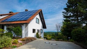 Una casa con techo solar, entrada pavimentada y vistas del paisaje circundante.