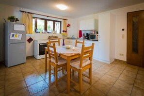 Una cocina compacta con una mesa de comedor y sillas, un refrigerador, un microondas y una ventana con cortinas.