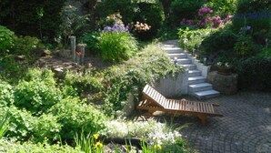 Un jardín con un banco de madera, escalones de piedra y diversas plantas.