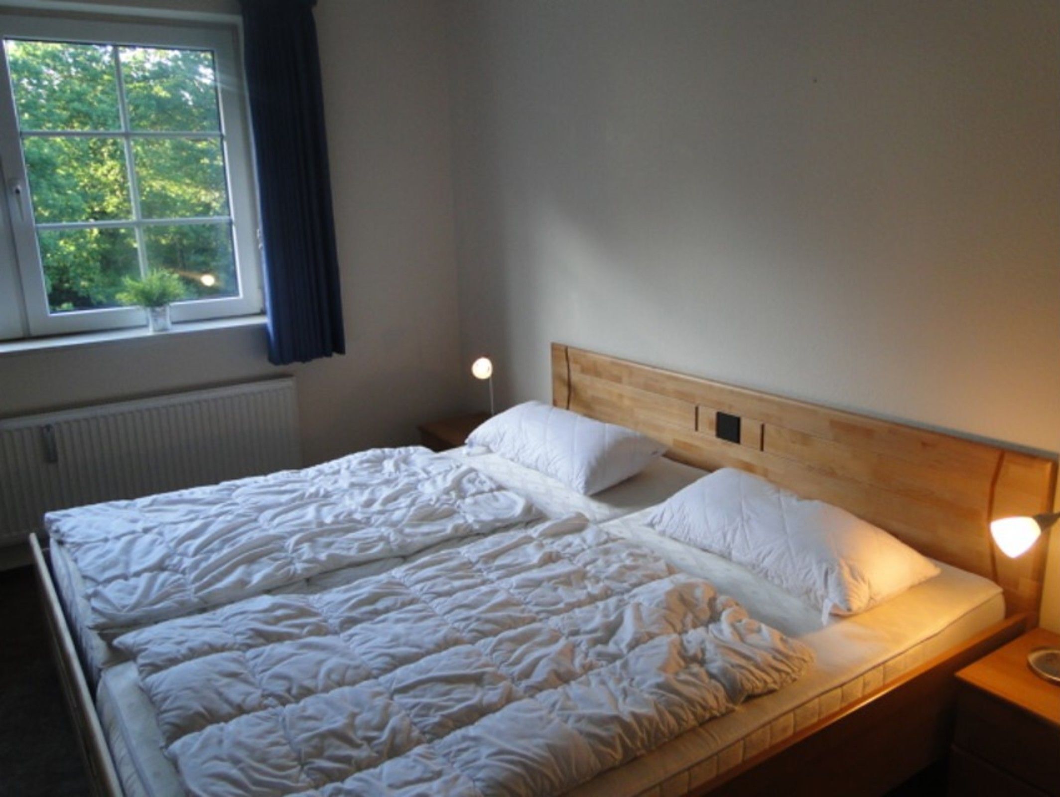A bed with white bedding, a wooden headboard, and bedside lamps.