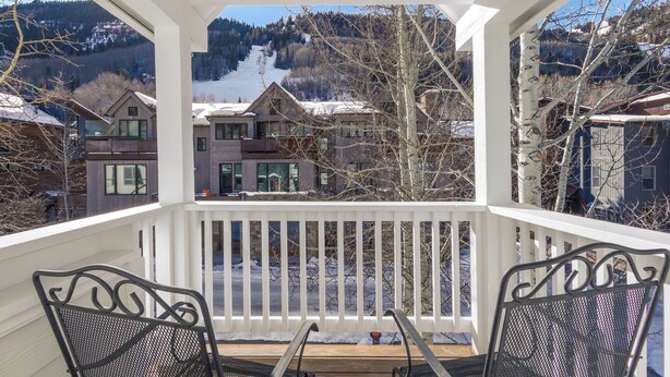 A covered outdoor area with two metal chairs and a wooden table, overlooking a snowy mountain and residential buildings. - SOUTH PACIFIC TOWNHOUSE- Walk to Gondola and Exquisite Mountain Views (Telluride)