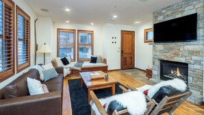 A cozy living room with a stone fireplace, leather sofa, wooden coffee table, and a flat-screen TV mounted on the wall. - SOUTH PACIFIC TOWNHOUSE- Walk to Gondola and Exquisite Mountain Views (Telluride)