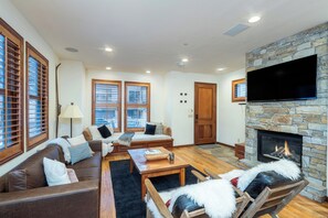 A living room with a stone fireplace, wooden furniture, and large windows with blinds. - Walk to Ski Downtown Telluride Townhome | Guest Favorite! Walk to Gondola & Town (Telluride)