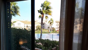 Ein Balkon mit Tisch und Stühlen, Blick auf einen Swimmingpool, Palmen und Wohnhäuser im Hintergrund.