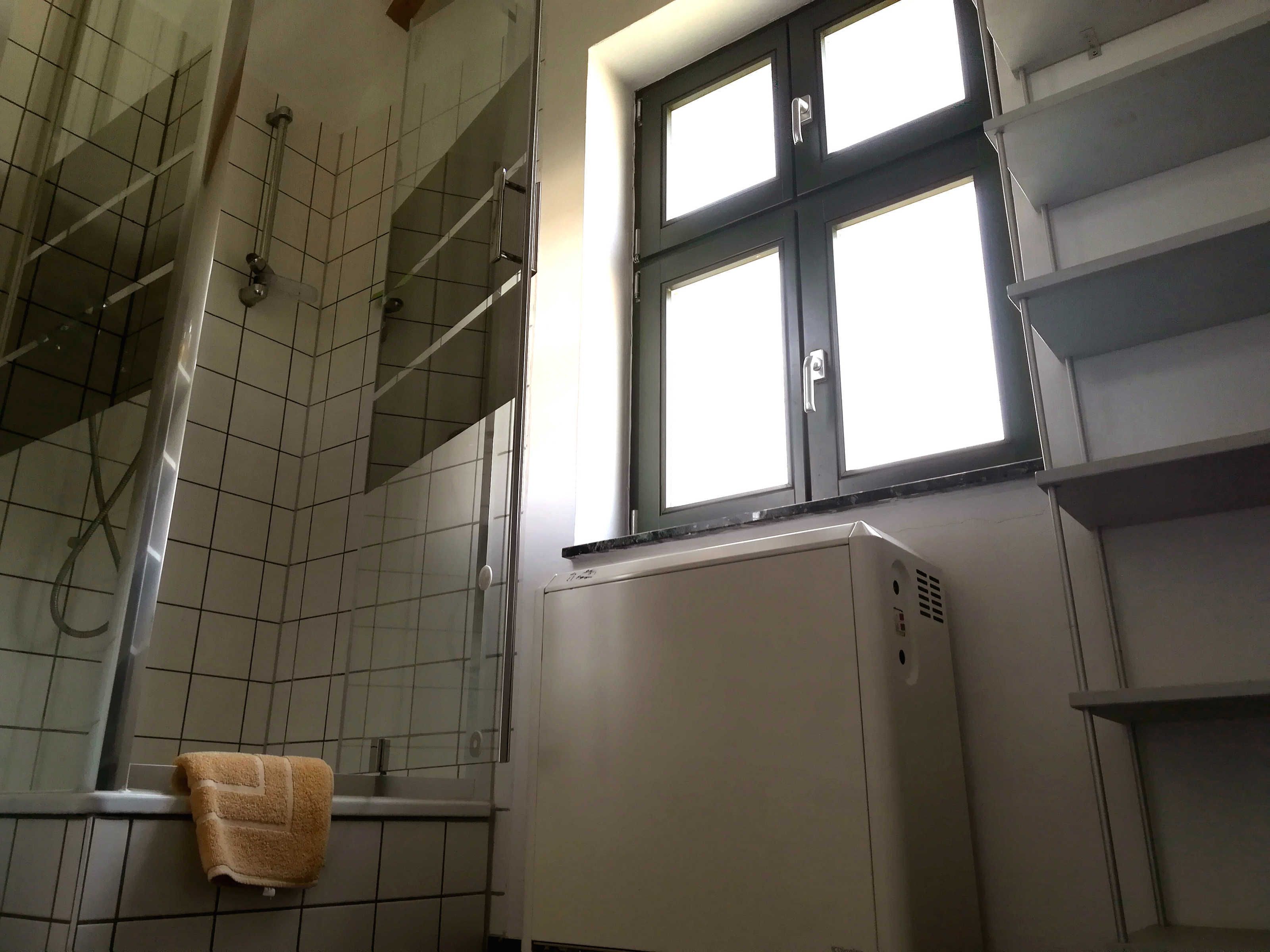 Un baño con suelo de baldosas, un perchero, una ventana y un calentador blanco.