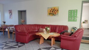 A living room with a red leather sofa, a wooden coffee table, and a patterned floor. - Single room (room 23) - Gästehaus EJS e. V.  Eggesin (Eggesin)