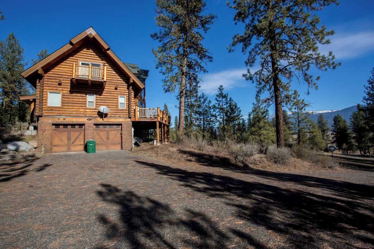A log cabin with a balcony, a garage, and a clear view of surrounding trees and mountains.