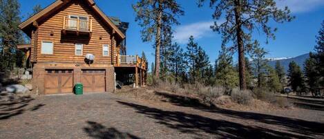 A log cabin with a balcony, a garage, and a clear view of surrounding trees and mountains.