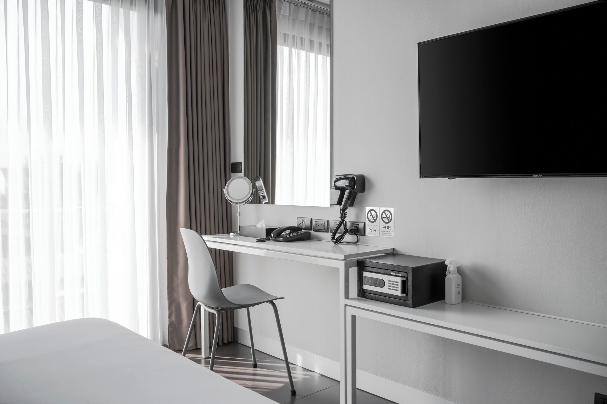 Habitación de hotel con cama, escritorio con silla, televisor de pantalla plana, ventana con cortinas y un minibar.