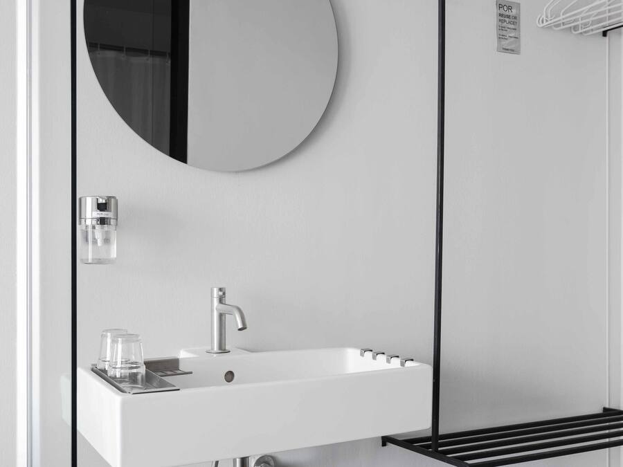 Un baño moderno con un lavabo blanco, un espejo redondo y un perchero para toallas.