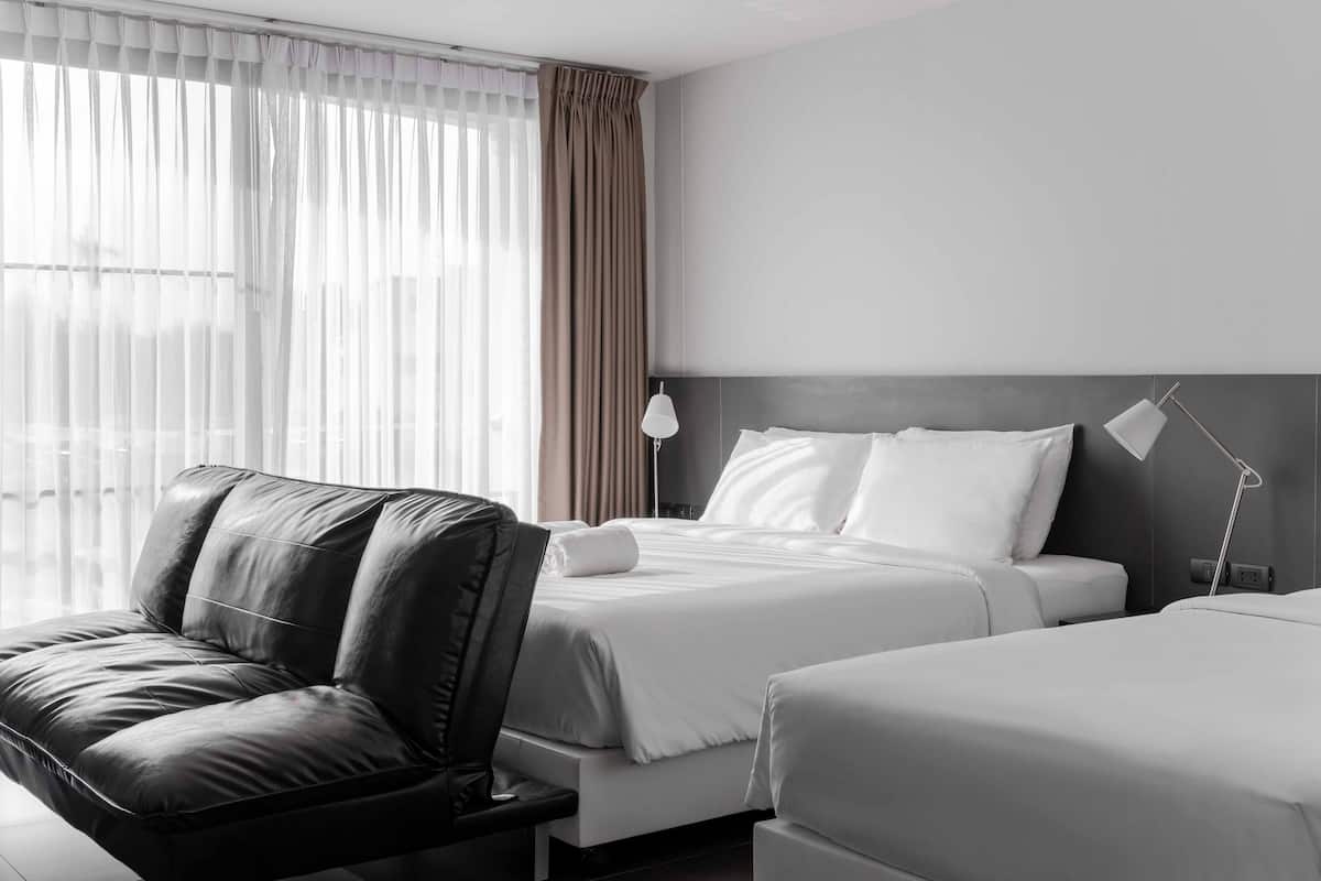 A hotel room with a bed, a leather sofa, and a bedside table.