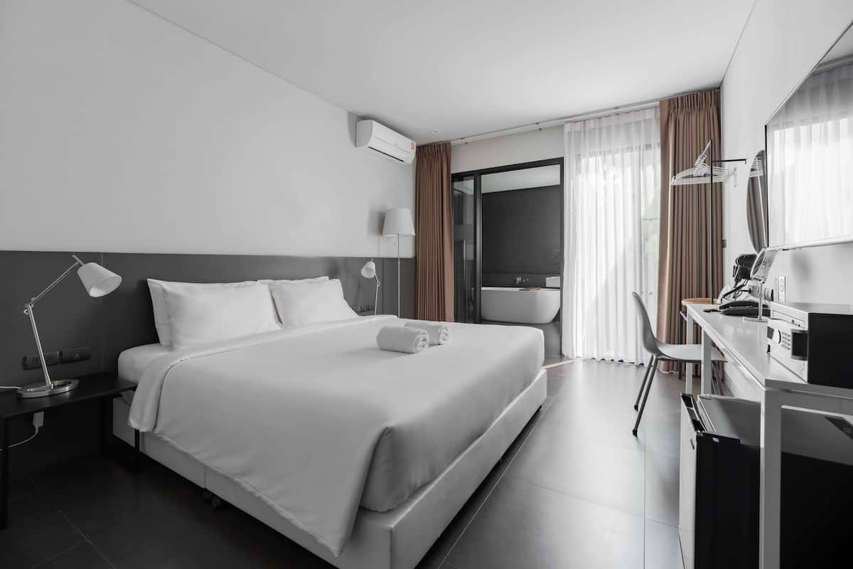 A modern hotel room with a large bed, a desk, a chair, a vanity, and a bathroom.