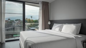 Une chambre d’hôtel avec un grand lit, une table de chevet et une vue sur le paysage urbain, visible à travers une grande fenêtre.
