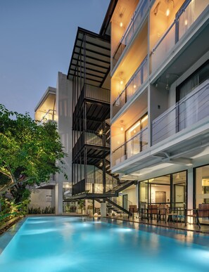 A modern hotel with a pool, outdoor seating, and a staircase leading to the upper floors. - POR Thapae Gate (Chiang Mai)