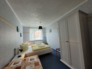 A bedroom with a bed, a chair, a wardrobe, a window with curtains, and a radiator. - Apartment 16 - Baltic Sea shell (Zinnowitz)