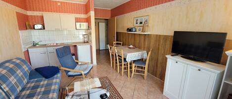 Een knus woongedeelte met een bank, een eettafel, stoelen, een televisie en een kitchenette.