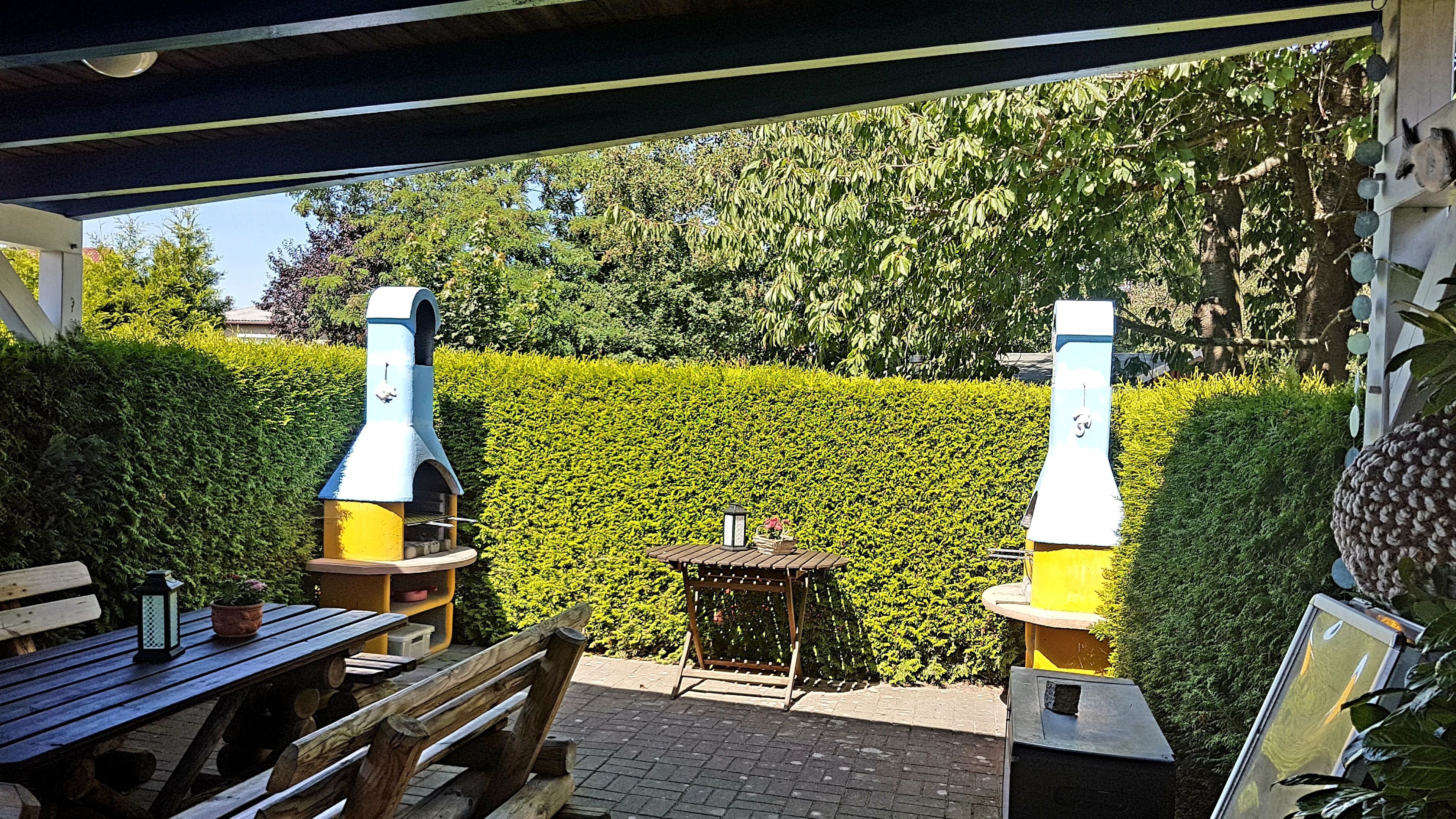 En terrasse med et træbord og bænke, et lille rundt bord med en lygte, samt to grill.