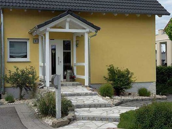 Keltainen talo, jossa on valkoinen kuisti, kiviporras ja pieni puutarha.
