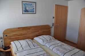 Une chambre à coucher avec une tête de lit en bois, un lit recouvert d’une literie à motifs, une table de chevet avec une lampe et une porte.