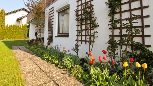 A white building with a brick roof, a wooden trellis, and a garden with red and yellow tulips. - NR vacation apartment no. 1, 2 persons - Holiday apartment Nain (Bad Dürrheim)