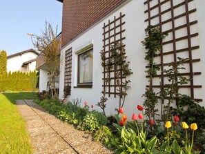 Un edificio blanco con techo de ladrillo, una ventana y una estructura de celosía. Hay un jardín con tulipanes rojos y amarillos y un camino de grava.