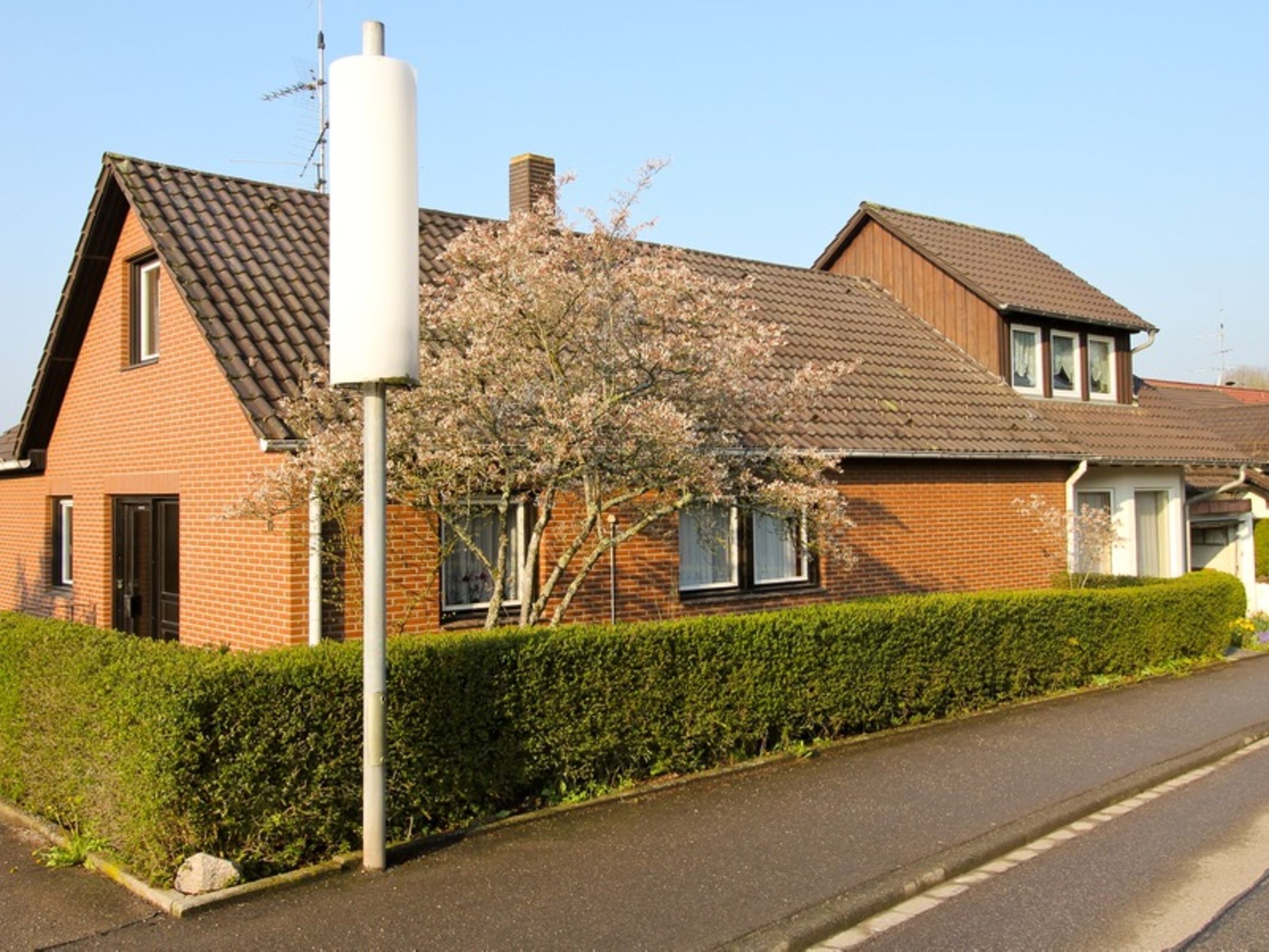 A two-story brick house with a tiled roof, a chimney, and a large white utility pole.