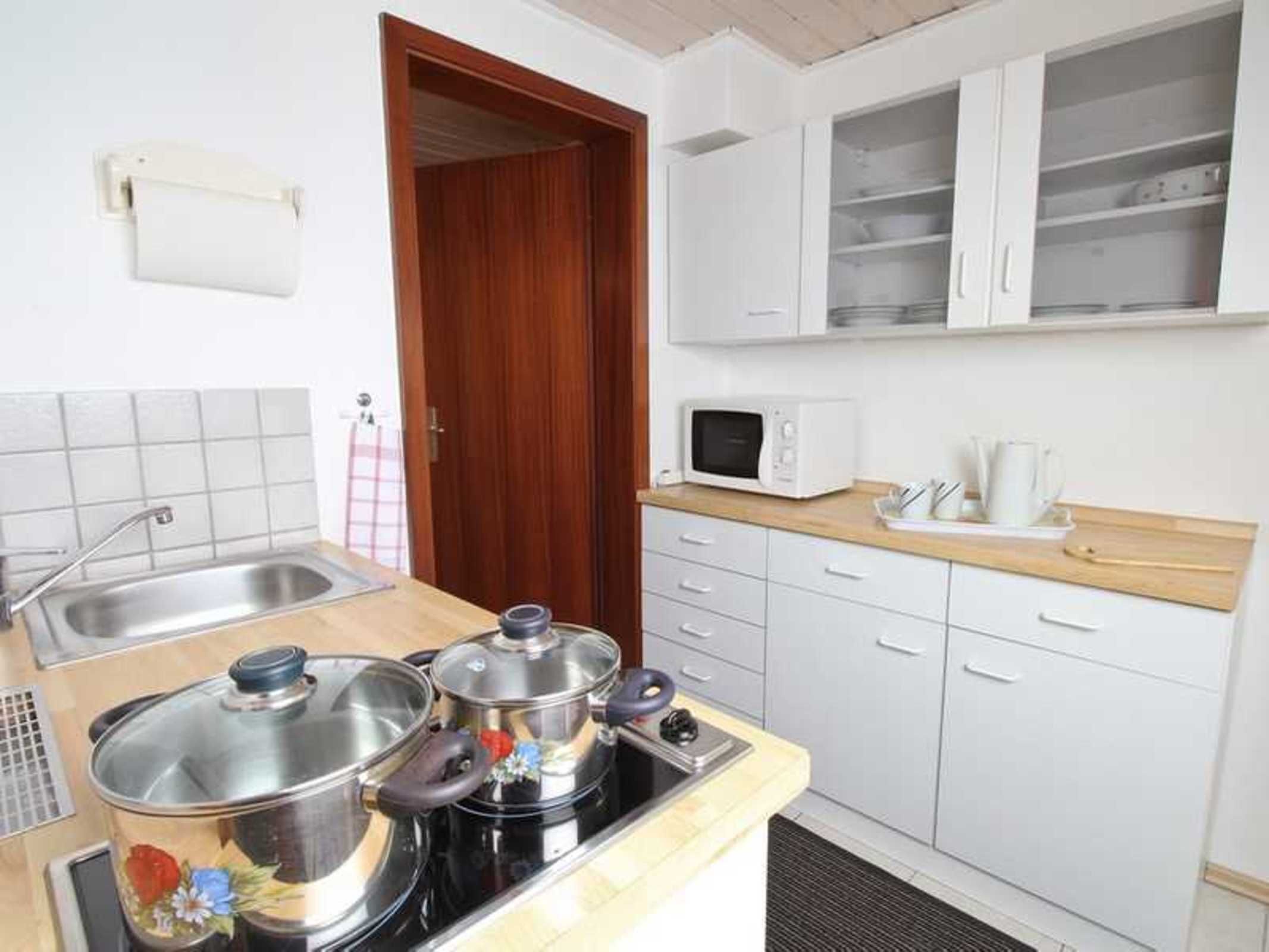 Una cocina funcional con estufa, ollas, microondas y fregadero.