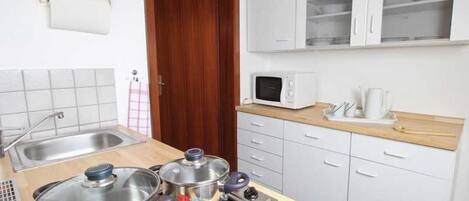 Una cocina funcional con estufa, ollas, microondas y fregadero.