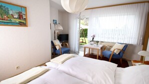 A hotel room with a bed, two chairs, a small table, a painting, and a window with curtains. - NR vacation apartment no. 1, 2 persons - Holiday apartment Nain (Bad Dürrheim)
