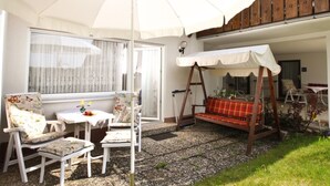 A patio with a white umbrella, a swing, and a table with chairs. - NR vacation apartment no. 1, 2 persons - Holiday apartment Nain (Bad Dürrheim)