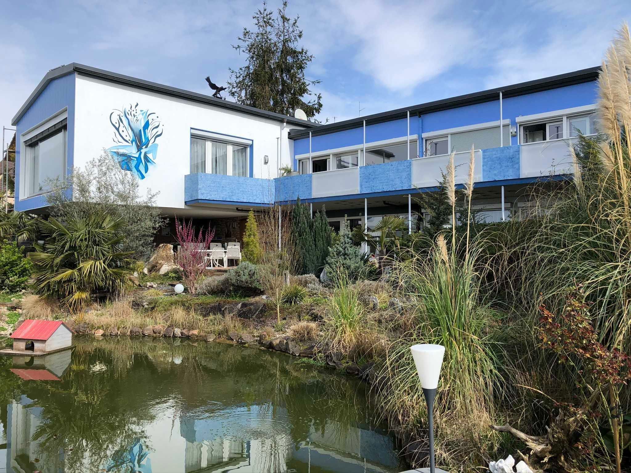 Ein modernes Gebäude mit einer blau-weißen Fassade, ein Teich im Vordergrund und ein Vogel auf dem Dach.