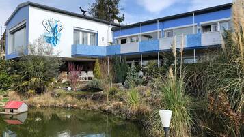 Ein modernes Gebäude mit einer blau-weißen Fassade, ein Teich im Vordergrund und ein Vogel auf dem Dach.