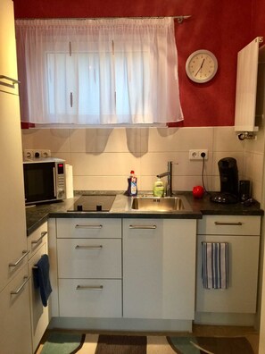 Eine kompakte Küche mit Mikrowelle, Toaster, Spüle und einer Uhr an der Wand.
