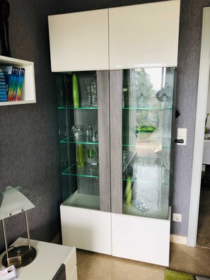 A modern room with a glass-fronted cabinet, a white desk, and a lamp.