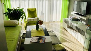Un salon moderne avec un fauteuil vert, un canapé, une table basse avec un livre, un téléviseur et une bibliothèque.