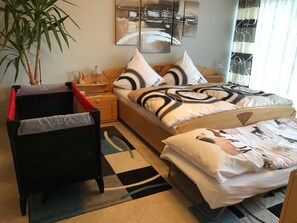 A bedroom with a bed, a chair, a nightstand, a lamp, a plant, and abstract wall art.