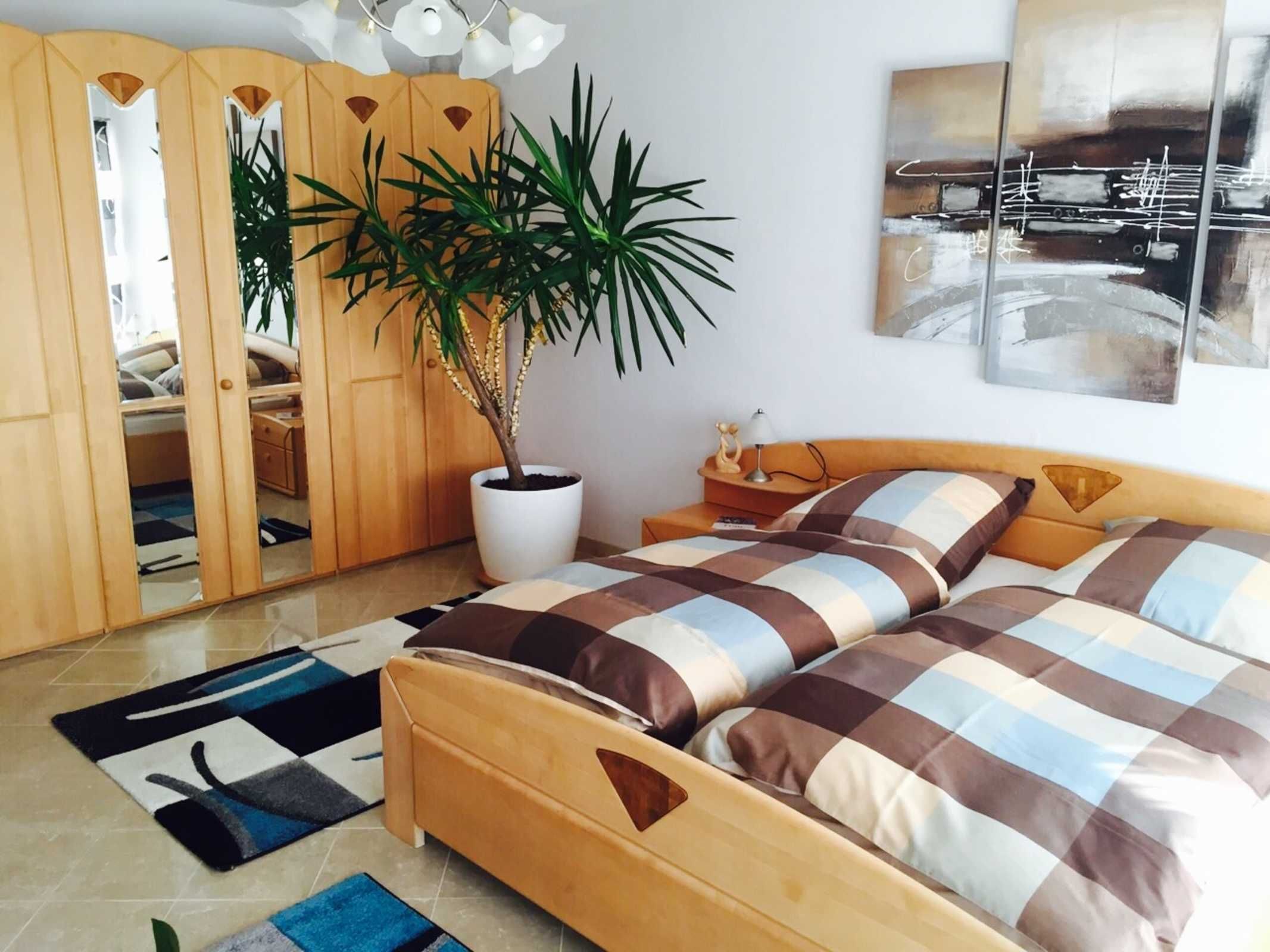 Ein Schlafzimmer mit einem Bett, einer Zimmerpflanze, einem Kleiderschrank und einem Bild an der Wand.