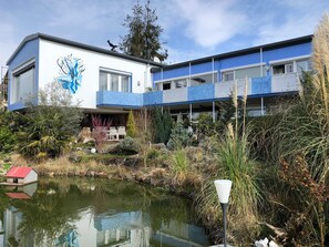 A modern building with a blue and white facade, a pond in the foreground, and a bird on the roof.