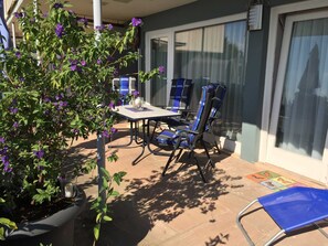 Eine Außenpatio mit Tisch, Stühlen, einem Blumentopf und einem Fenster mit Jalousien.