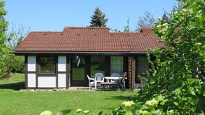 Una casa pequeña con techo de tejas, un patio con mesa y sillas, y un jardín al frente.