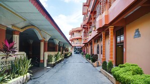 A corridor with a covered walkway, potted plants, and a building with balconies and windows.