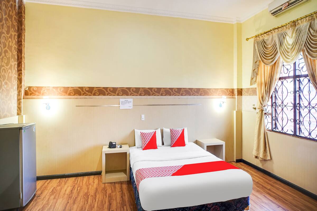 Ein Hotelzimmer mit Bett, Nachttischen, einem Schreibtisch, einem Kleiderschrank und einem Fenster mit Vorhängen.