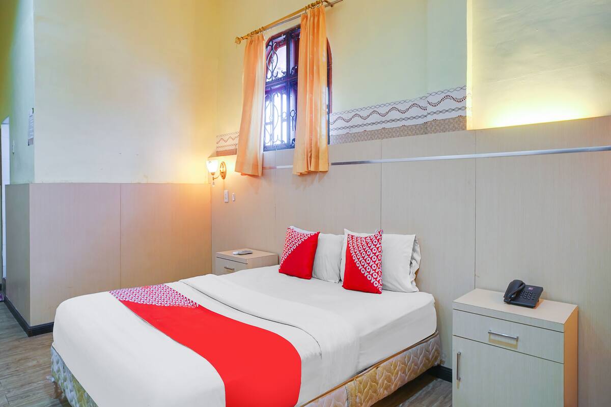 Ein Hotelzimmer mit Bett, Nachttisch, Telefon und einem Fenster mit Vorhängen.