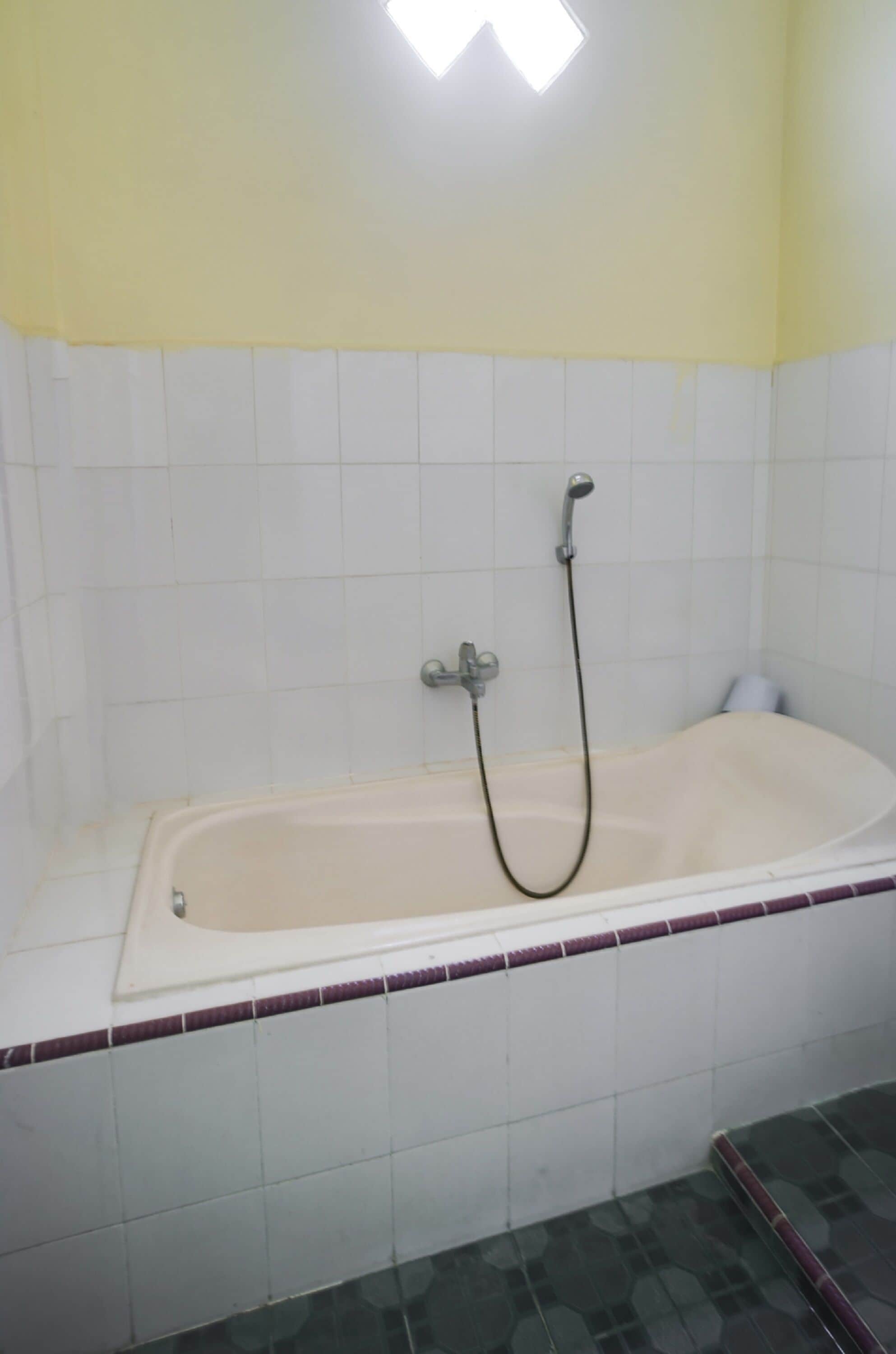 Un baño con bañera, paredes de azulejos blancos y techo amarillo.