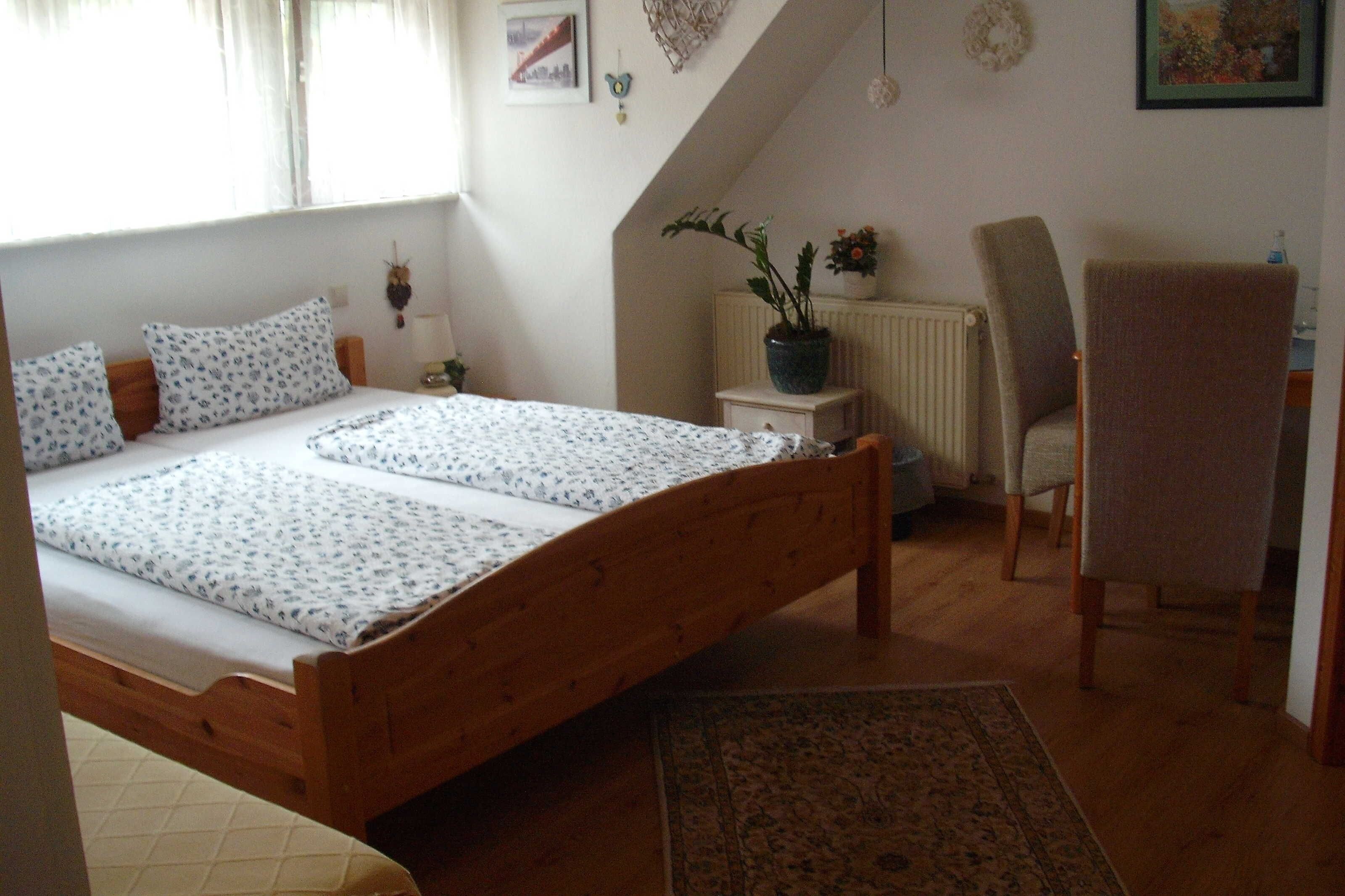 A bedroom with a wooden bed, a chair, a radiator, and a potted plant.