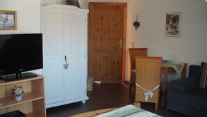 A room with a television, a wardrobe, a dining table with chairs, and a sofa.